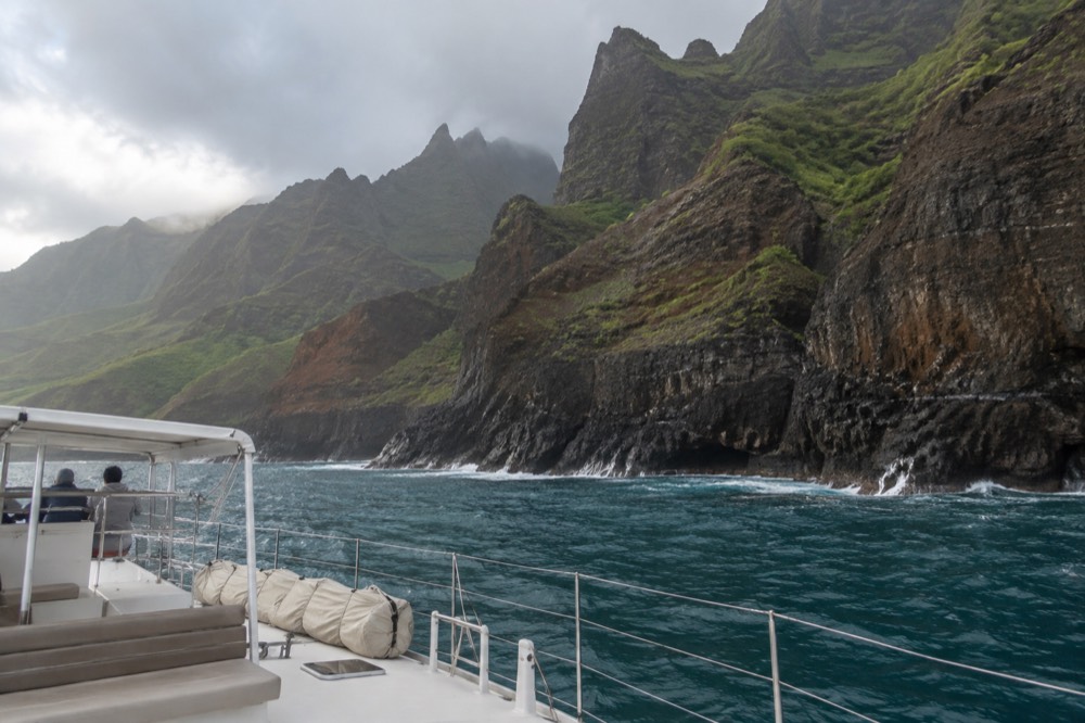 A power catamaran cruising close to the green sea cliffs of the Napali Coast