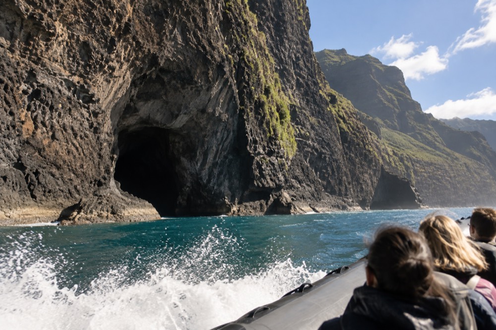 A rigid-hull inflatable raft running along the Napali cliffs near a sea cave opening