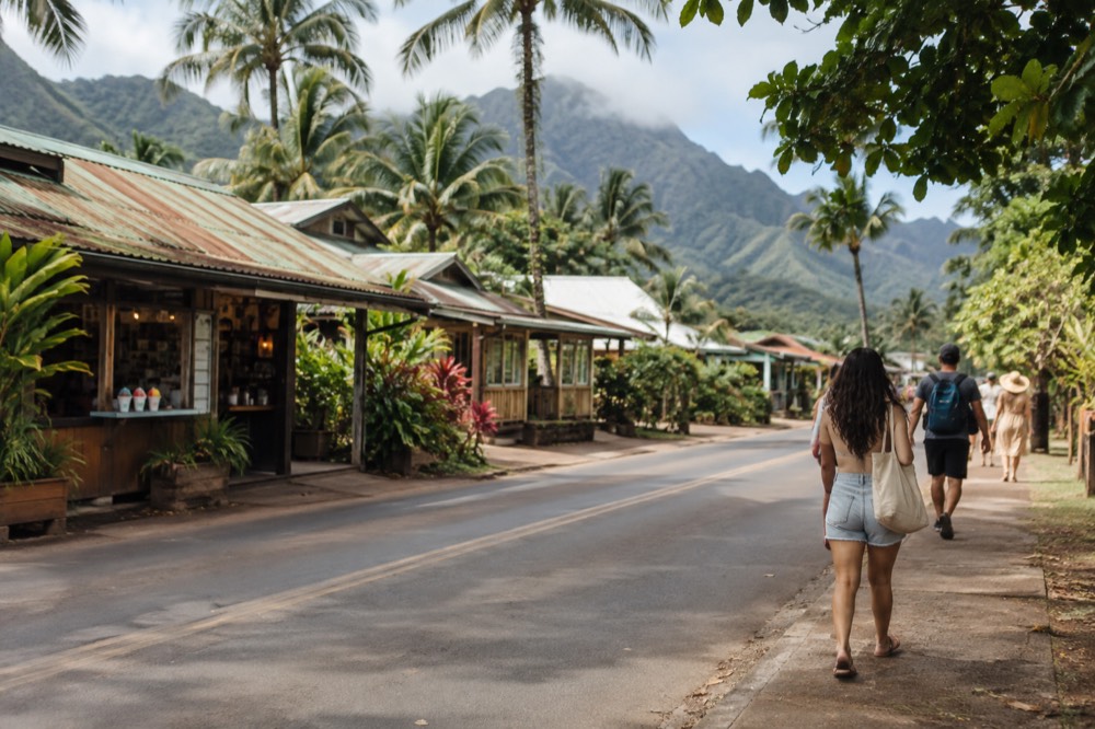 A small town street with low storefronts and palm trees along a coastal highway.