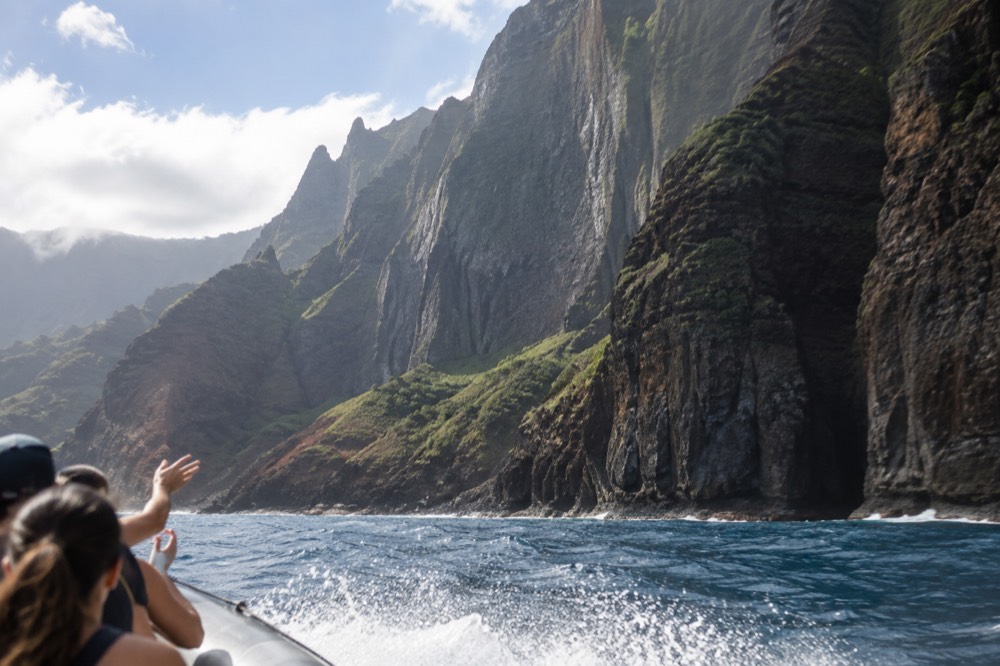 A small inflatable raft cruising close beneath tall coastal cliffs
