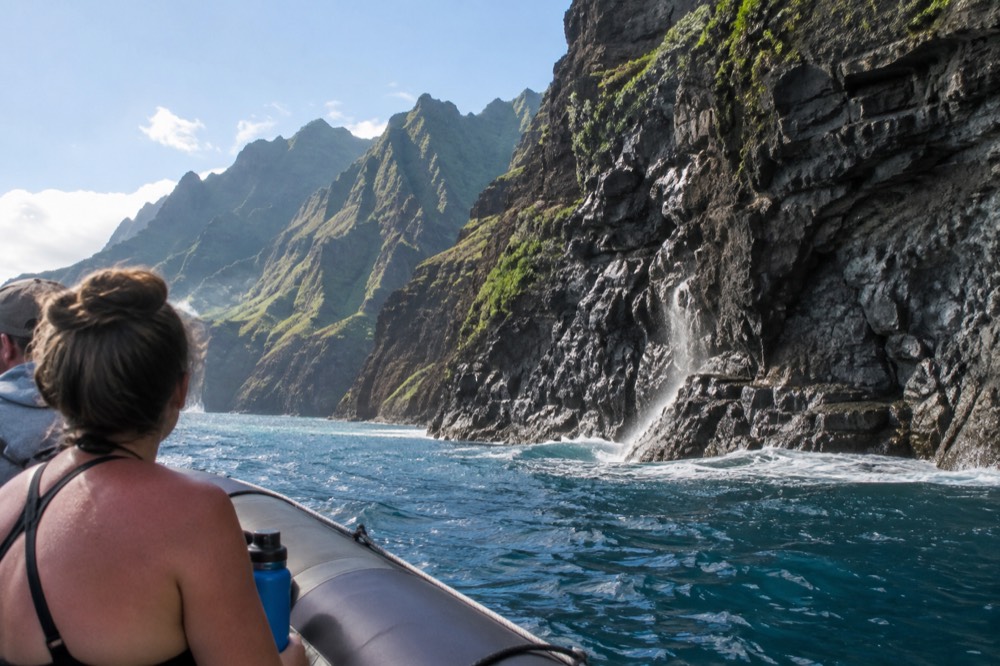 A rigid-hull inflatable raft cruising close to tall green sea cliffs