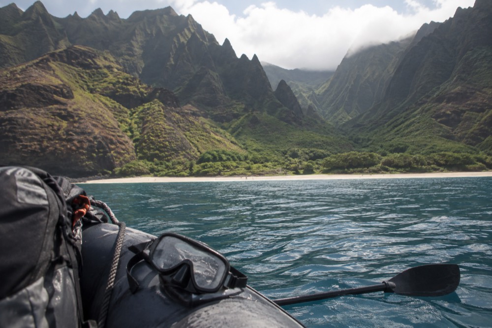 A small raft cruising close to tall Napali sea cliffs with greenery above the waterline