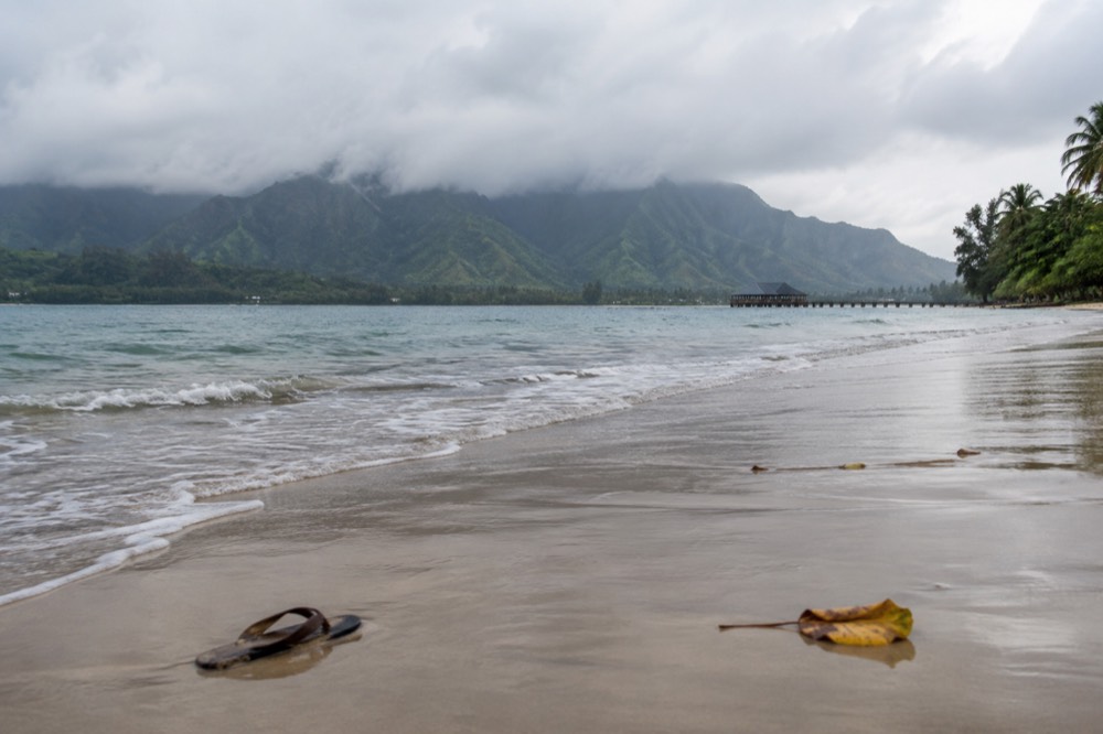 A calm Hanalei Bay with green mountains behind a long sand beach