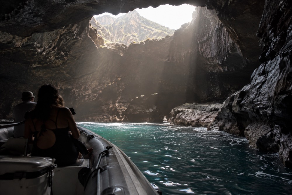 A raft floating inside a wide sea cave with light entering through a collapsed ceiling