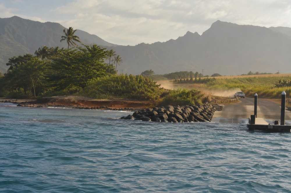 A coastal road curving along a green Kauai shoreline with a harbor town in the distance
