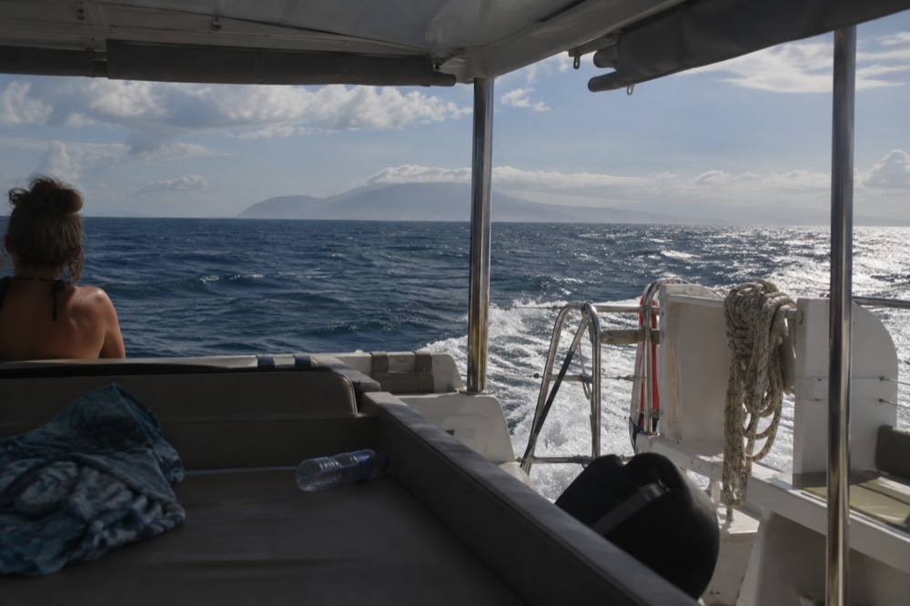 A catamaran underway on open ocean with a distant island on the horizon