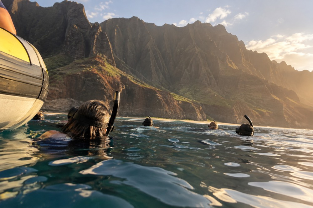 A small-group raft drifting with snorkelers in the lee of the Napali Coast cliffs