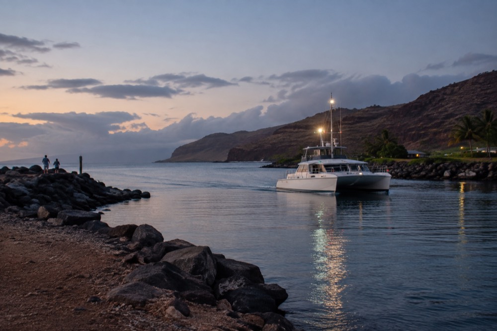 A small boat harbour at dusk with masts and a calm parking area beside the water