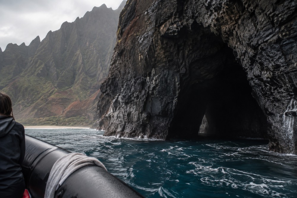 A rigid inflatable raft riding close to a dark rock sea cave opening