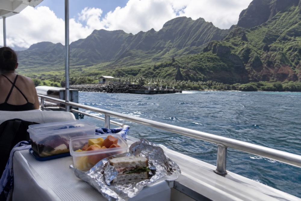 Lunch boxes open on a boat deck anchored off the green valley shore at Milolii on Kauai's Napali Coast