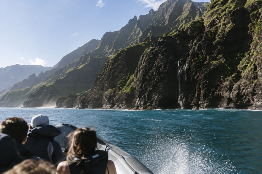 A rigid inflatable raft cruising along green Napali cliffs in morning light