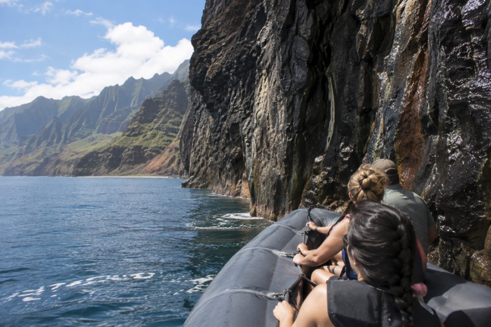 A rigid inflatable raft cruising close to a dark cliff face above calm water