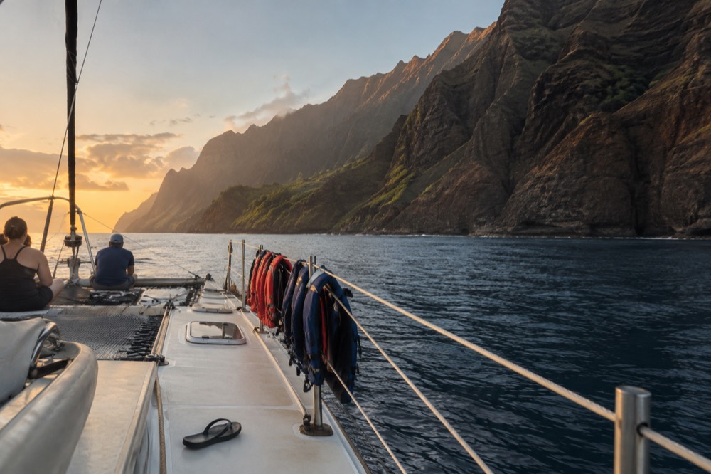 Close along a catamaran's stable twin hulls on flat water below the Napali Coast cliffs