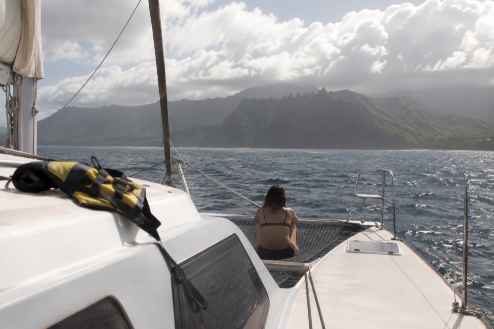 A catamaran under way on open water with cloud banks over distant Kauai cliffs