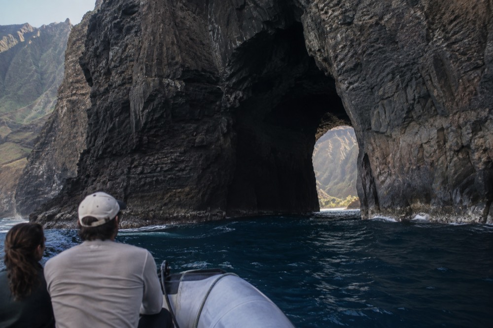 A small raft drifting near a dark sea cave opening in the Napali cliffs