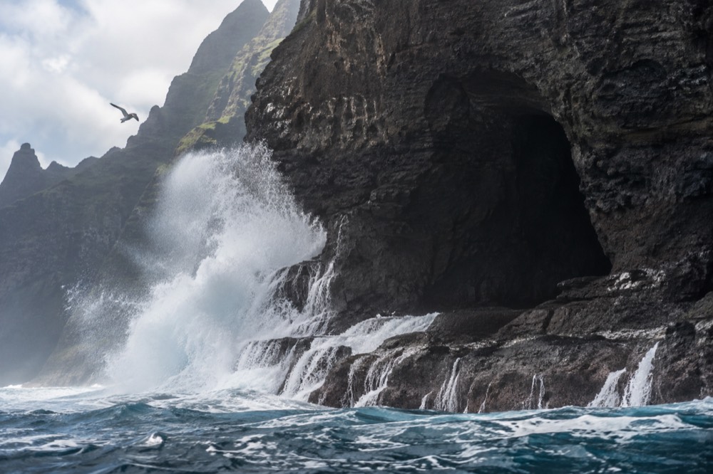 Ocean swell breaking against a dark cliff wall near a cave mouth