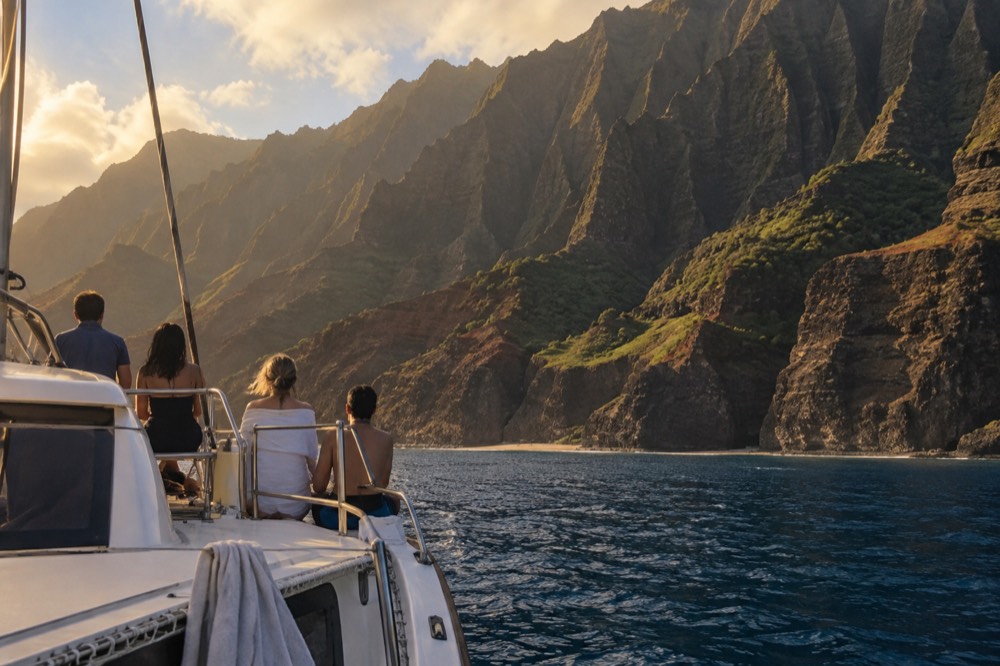 A catamaran anchored close to green sea cliffs with people on deck