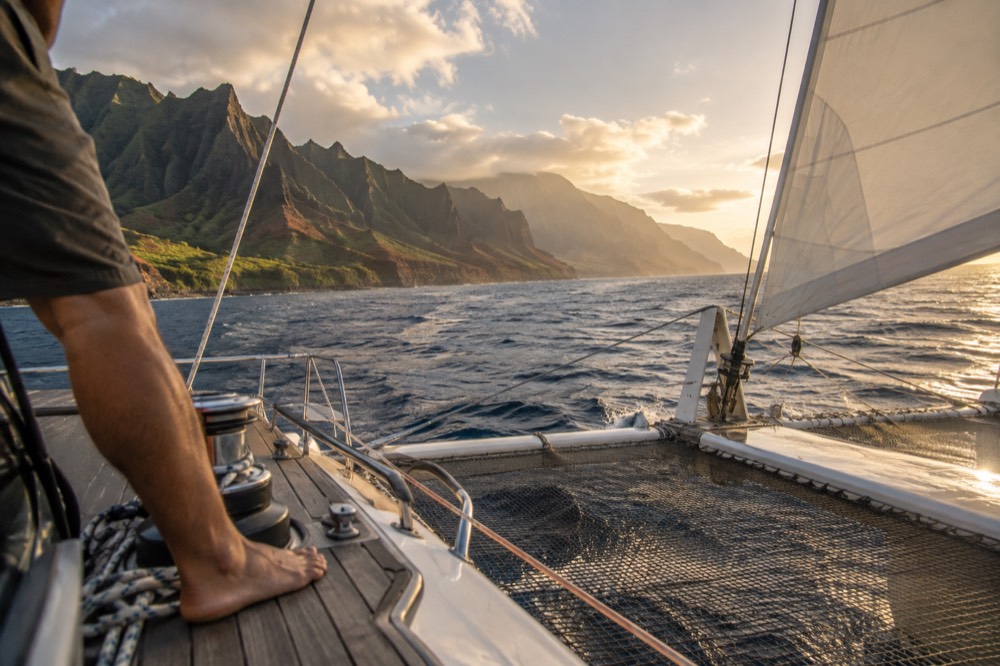 A catamaran under sail along the Napali cliffs in warm late afternoon light