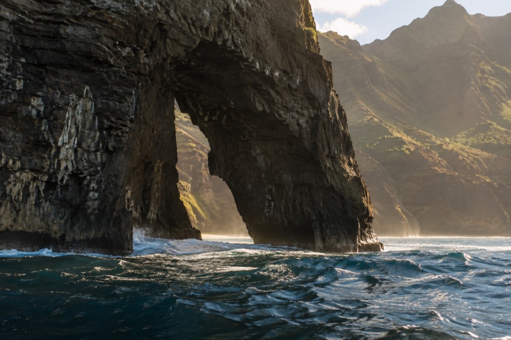 Sea cliffs and a rock arch along the Napali Coast seen from open water