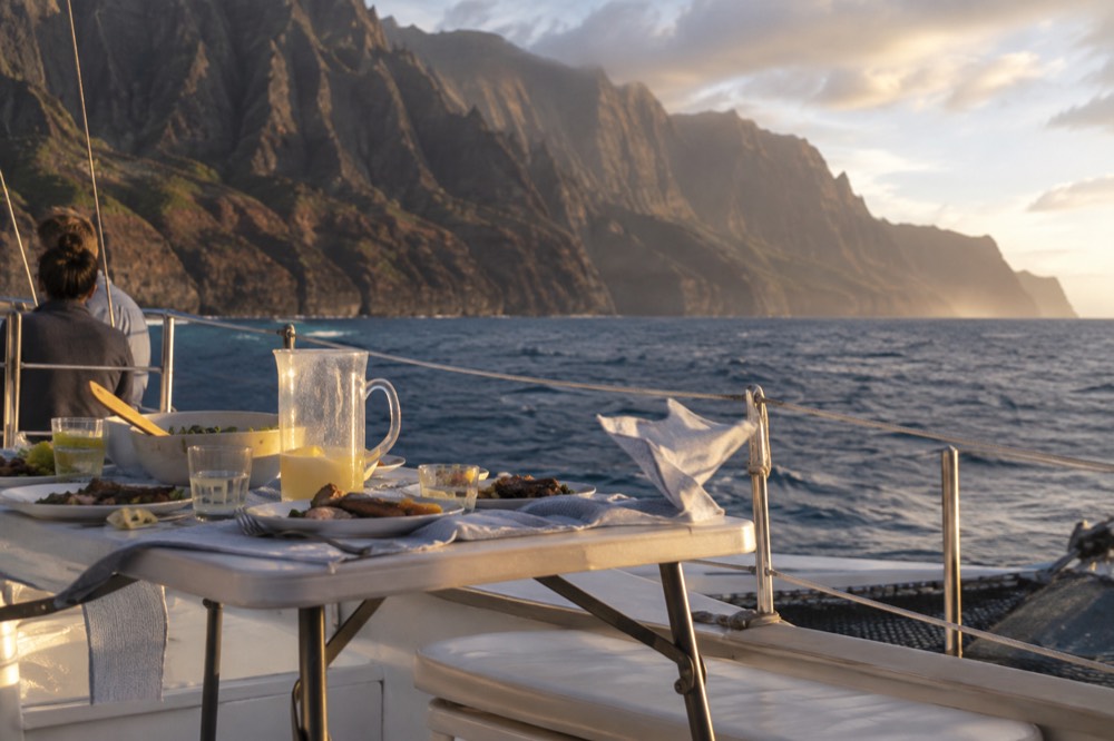 A dinner table set on the deck of a catamaran near the Napali shoreline