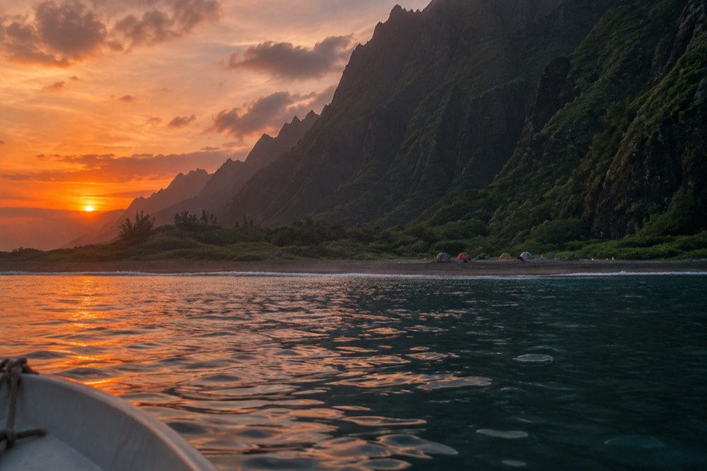 A small boat anchored near a Napali valley as the sun sets over the Pacific