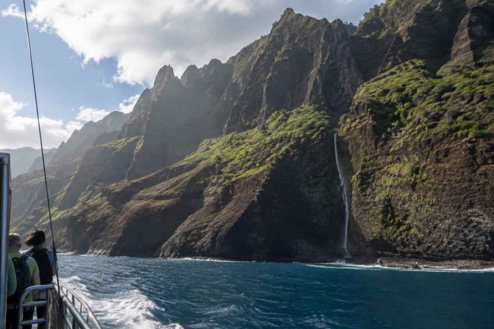 A catamaran cruising close to tall green sea cliffs along the Napali Coast