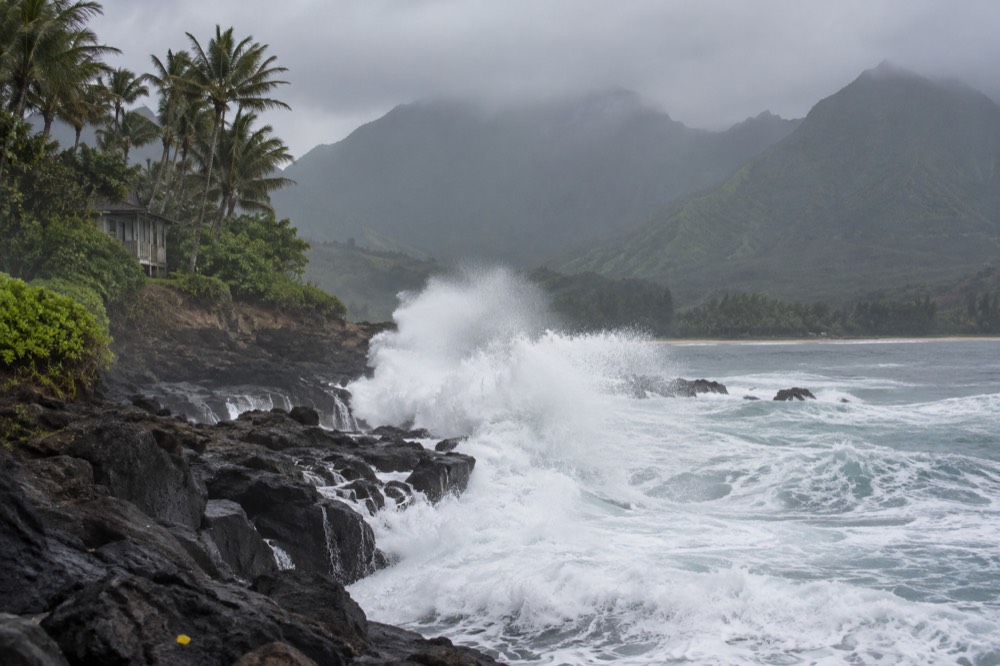 Large ocean swells breaking against a dark volcanic coastline under a grey sky