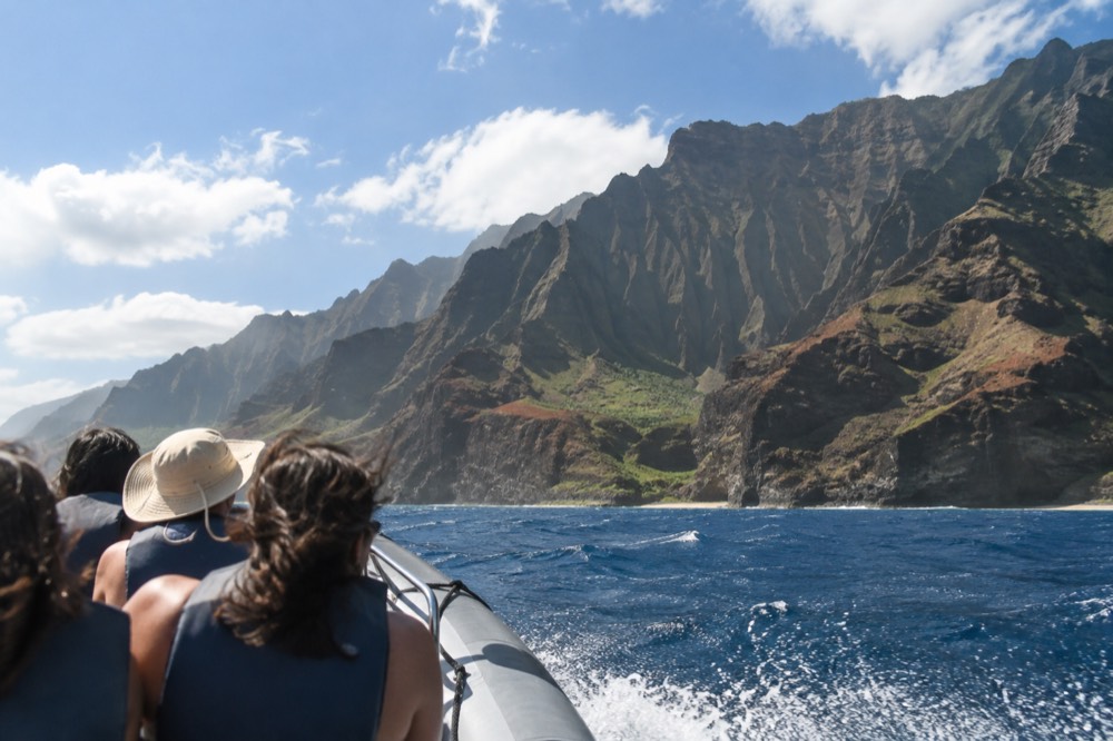 A rigid inflatable boat with passengers in life jackets speeding across open ocean toward tall sea cliffs