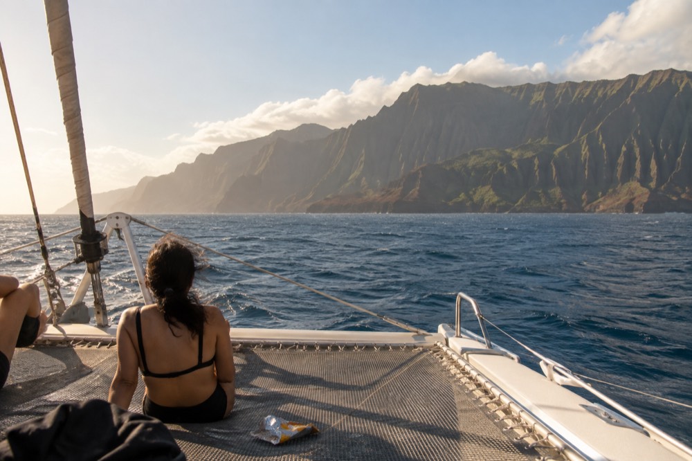 A catamaran underway on open water with Napali Coast cliffs on the horizon in the distance