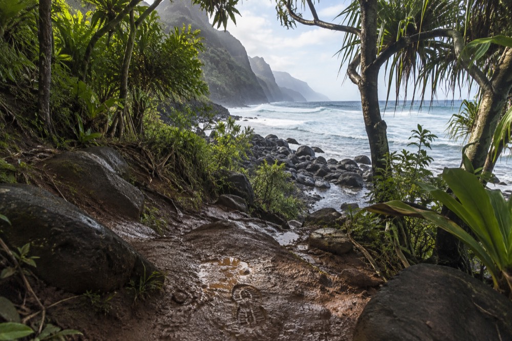 Mud-slick red-dirt trail drops toward Hanakapi'ai Beach on Kauai's north shore