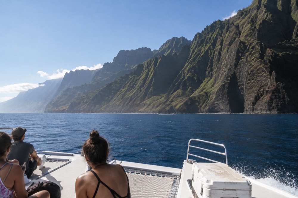 A power catamaran cruising past tall green sea cliffs on an open ocean horizon