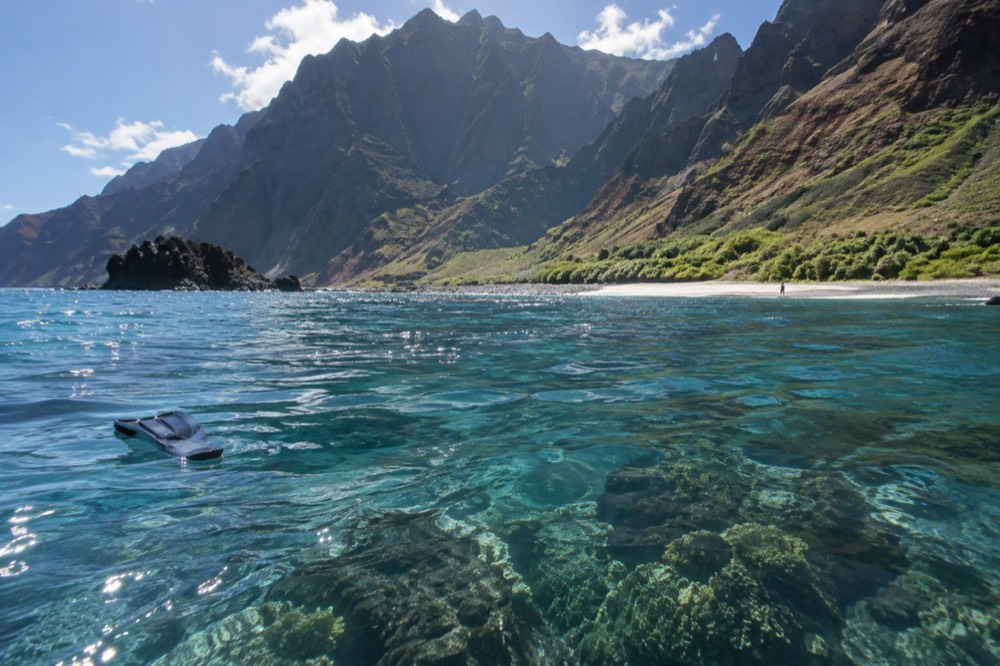 Clear turquoise water over a volcanic reef with a rocky islet in the background