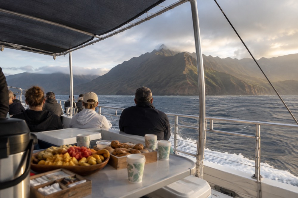 A catamaran deck with a served breakfast spread and passengers seated under shade