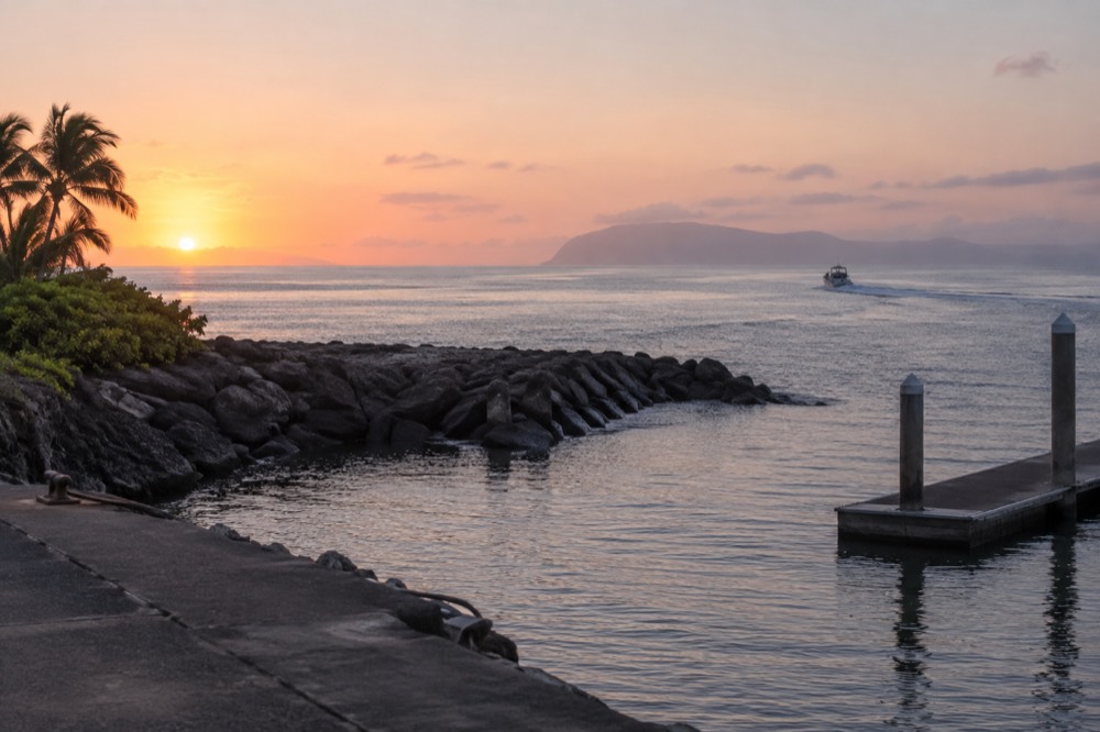 A calm open ocean channel at sunrise with a distant island on the horizon