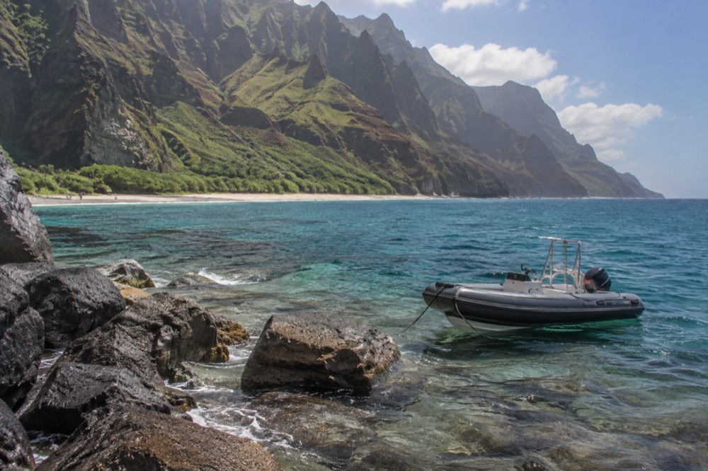 A rigid inflatable raft holding position near a rocky landing in clear tropical water