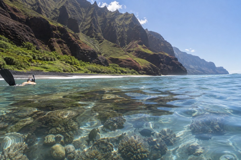 Calm shallow reef water over coral beside a dark sand beach