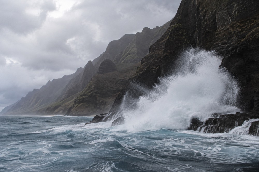 Large ocean swell breaking white against dark volcanic cliffs
