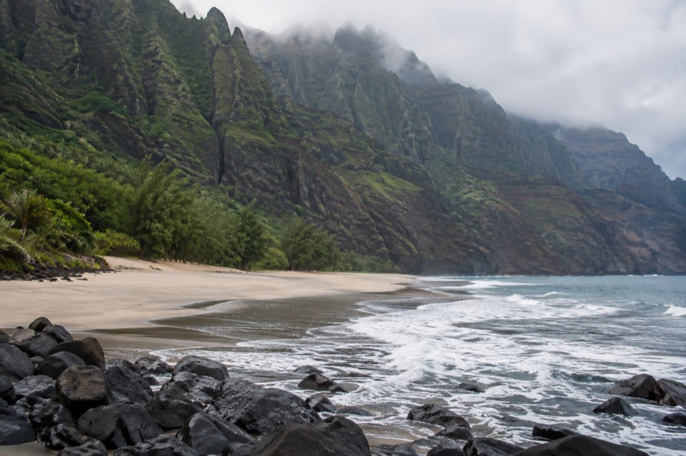 Shot from the far shallows, the whole landing beach of Nualolo Kai lies empty below its green cliff walls