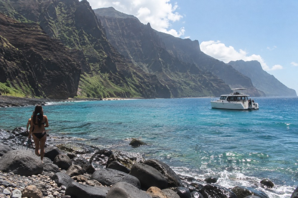 A power catamaran anchored near a reef in clear turquoise water along a green coastline