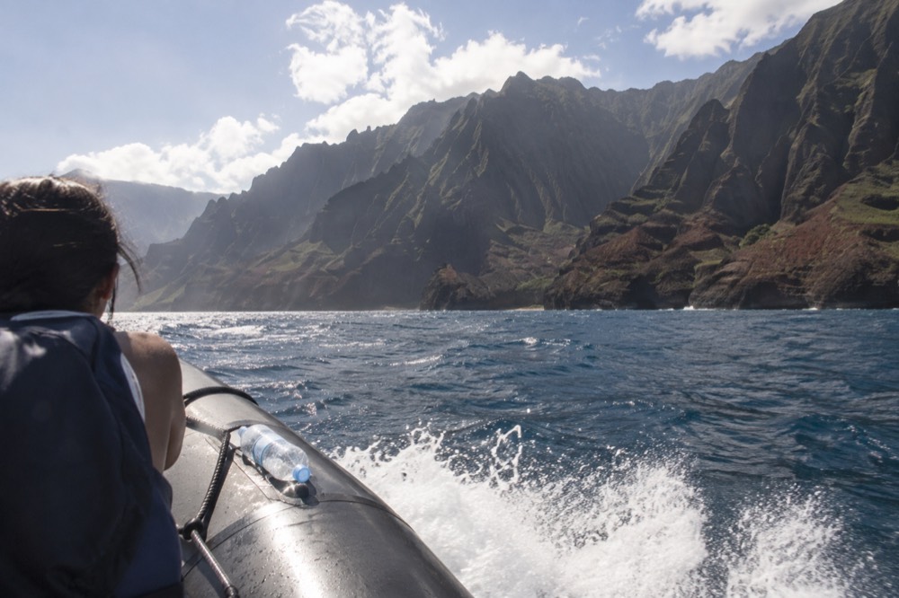 A small raft cutting through open water with spray rising near distant coastal cliffs