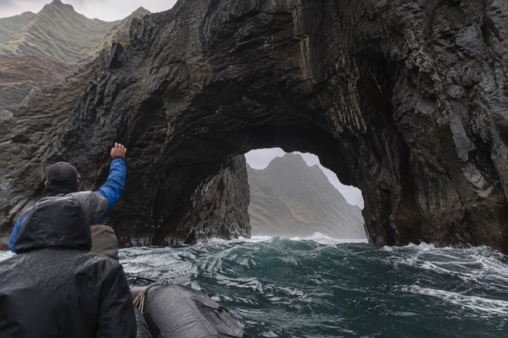 A raft holds at the water-level mouth of a sea cave beneath Honopu Arch